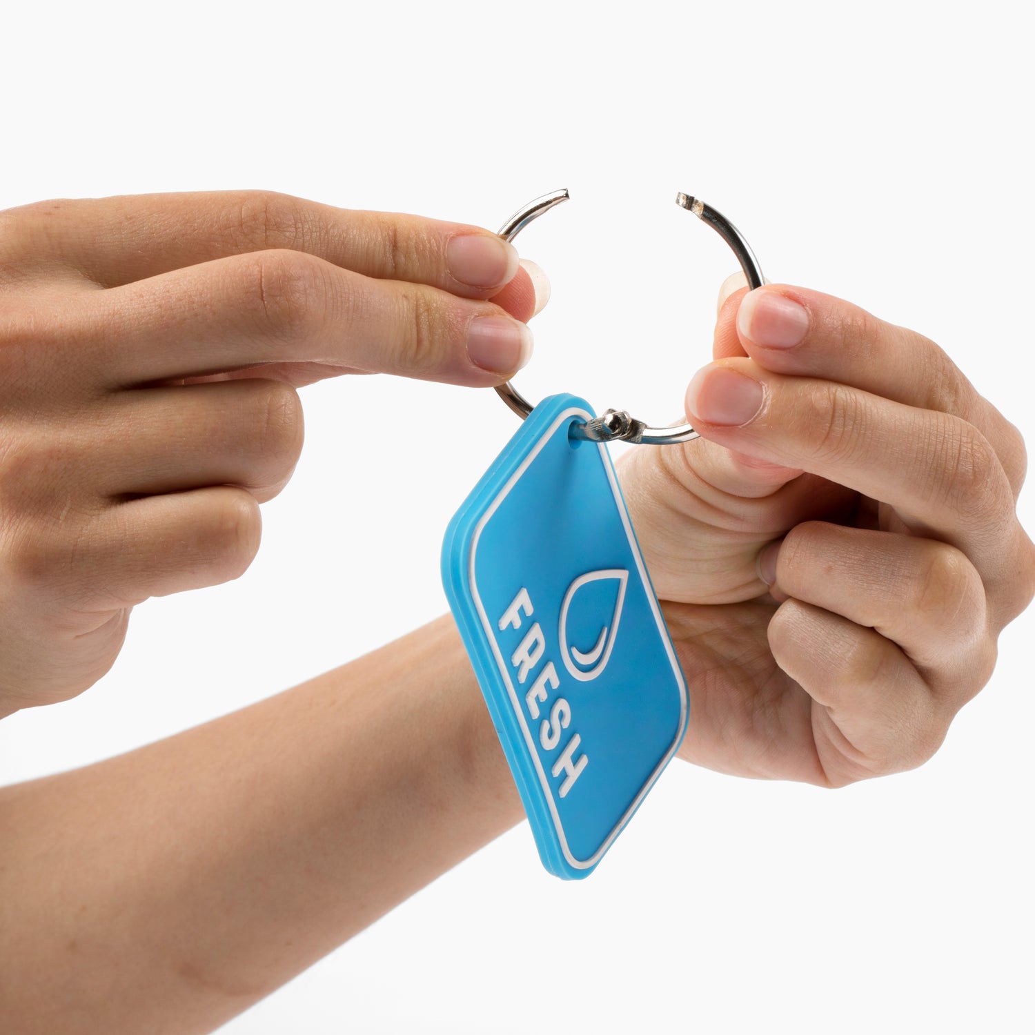 Hands attaching a blue 'Fresh' label to a metal ring, demonstrating the labeling system for RV hose bags. This essential RV accessory helps in organizing hoses by clearly marking them for fresh water use. Ideal for travel trailers and mobile homes, these labels prevent hose mix-ups and contamination. The labeled hose bags are crucial camper accessories for RV camping, ensuring proper identification and maintaining cleanliness in RV supplies
