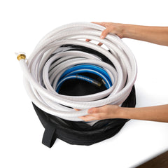 Hands placing coiled white and blue hoses into an RV hose bag. The image demonstrates the bag's capacity to hold multiple hoses, keeping them neatly organized. This essential RV accessory is ideal for travel trailers and mobile homes, helping to prevent contamination and maintain cleanliness. The hose bag is a crucial camper accessory for RV camping, offering a practical and efficient solution for hose storage.