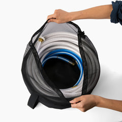 Hands holding open an RV hose bag containing coiled white and blue hoses. The image highlights the bag's capacity and mesh top for airflow, ensuring hoses remain dry and organized. This essential RV accessory is perfect for travel trailers and mobile homes, preventing contamination and maintaining cleanliness. The hose bag is a crucial camper accessory for RV camping, providing a convenient and effective solution for hose storage.